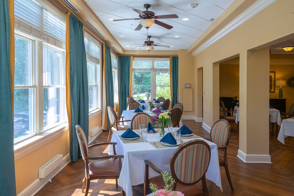 A well-lit dining room with elegant table settings, surrounded by large windows and blue curtains.