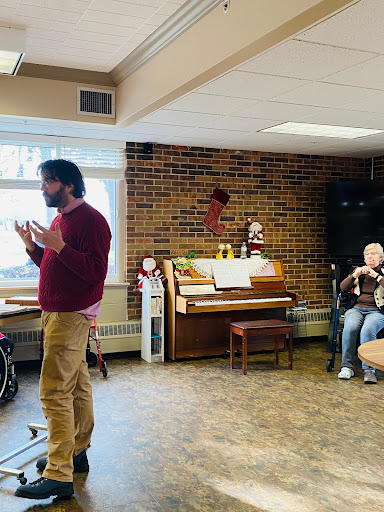 A speaker engages with an audience in a cozy indoor setting, accompanied by a piano.