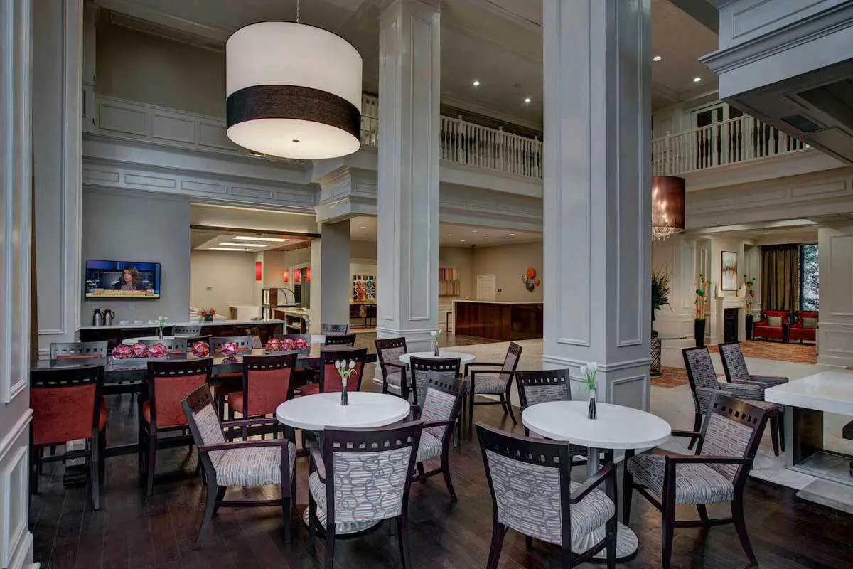 A modern restaurant interior with a dining area featuring several tables and chairs, a bar, and stylish lighting.