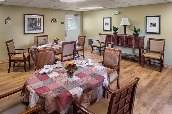 A cozy dining room with neatly arranged tables and chairs, featuring floral centerpieces and warm decor.