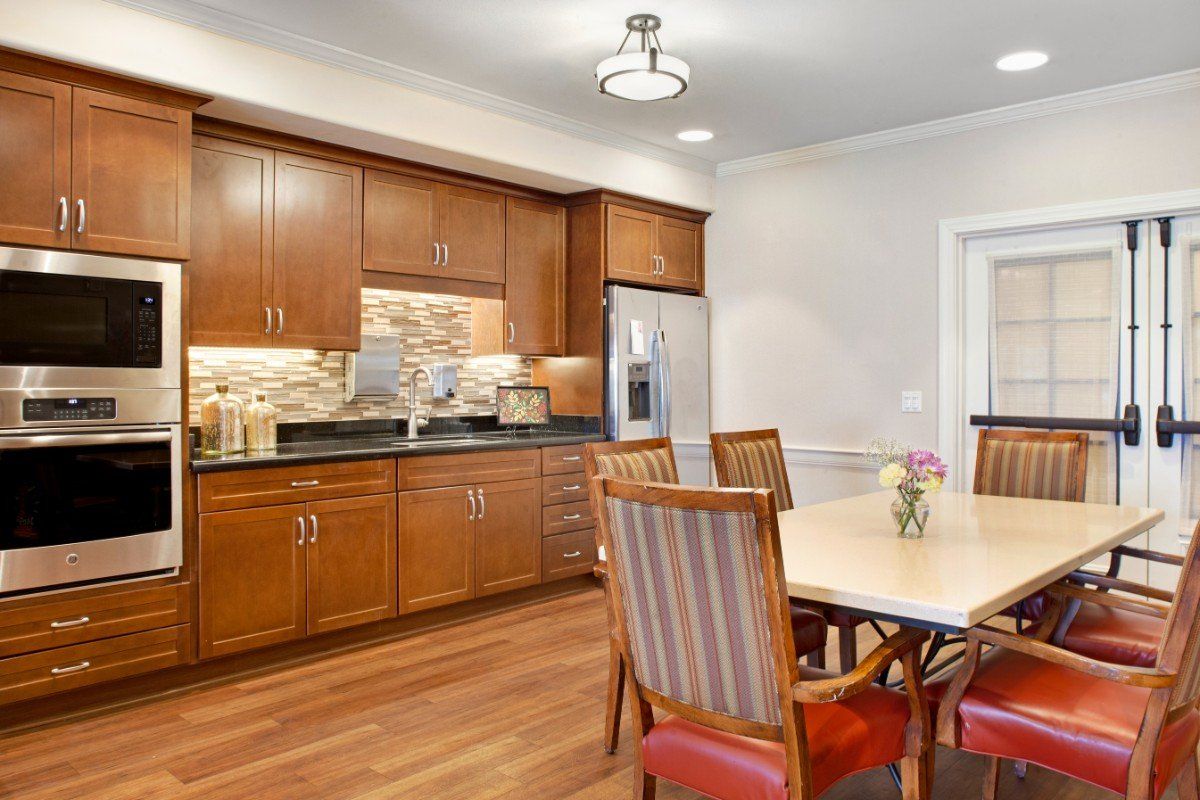 A cozy kitchen and dining area with wooden cabinets, hardwood flooring, and a modern light fixture.