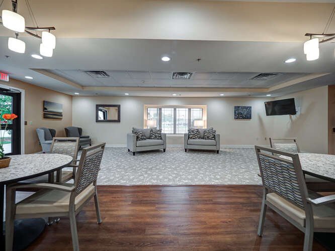 A comfortable lounge area with seating and tables, featuring a mix of carpet and hardwood flooring.