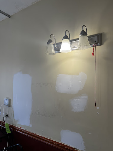 A wall featuring a modern light fixture, with areas of the wall showing uneven paint patches.
