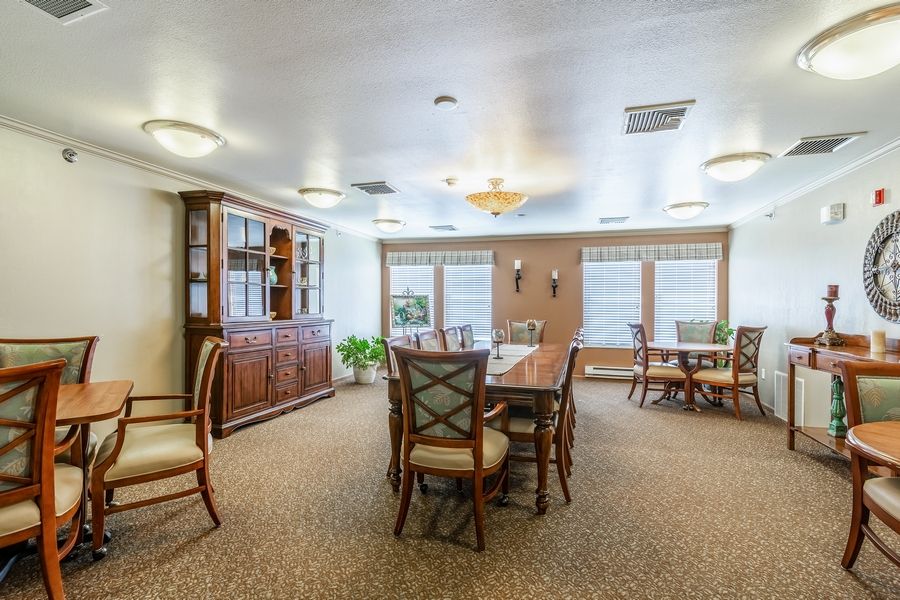 A spacious dining area with tables and chairs, well-lit by ceiling lights, featuring large windows and a wooden cabinet.