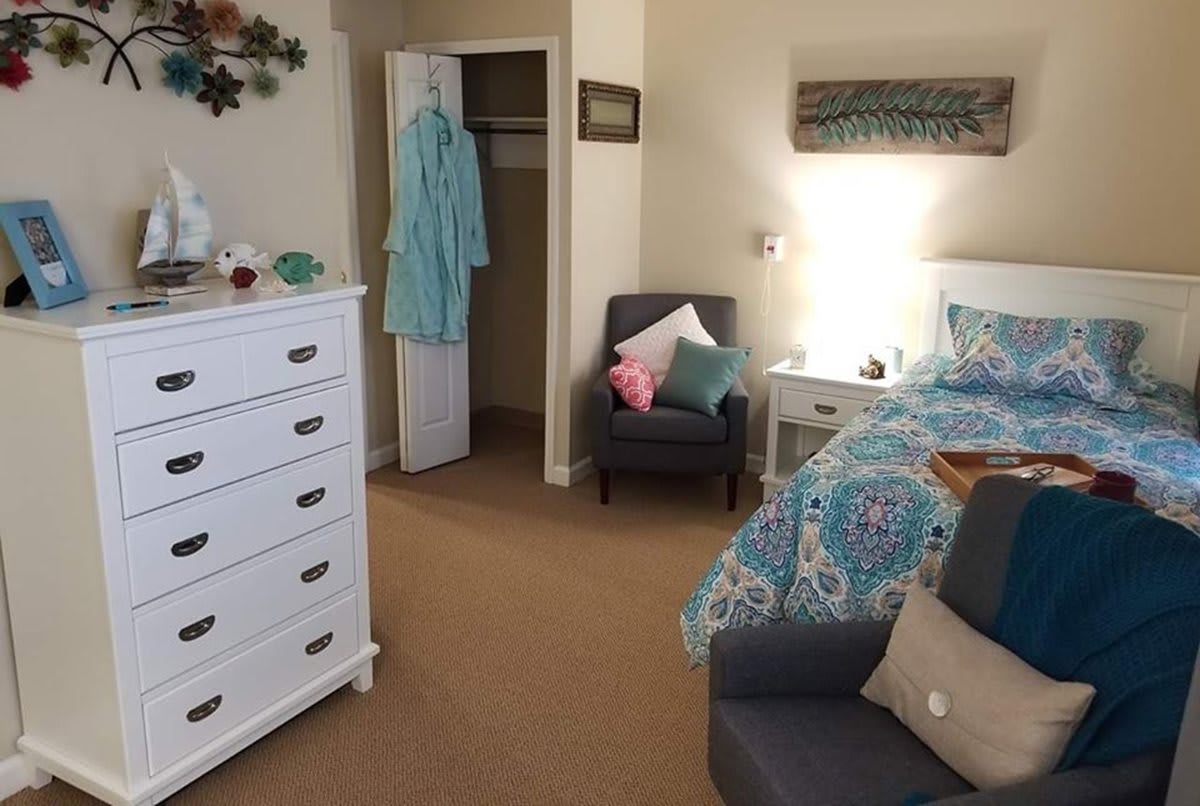 A cozy, well-decorated bedroom with a bed, chair, and dresser.