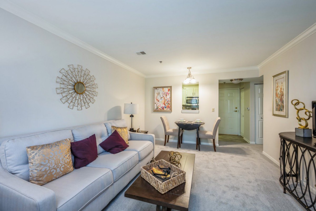 A cozy living room with a sofa, coffee table, and adjacent dining area featuring modern decor and artwork.