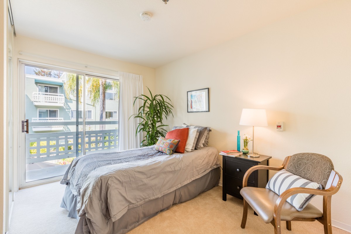 A cozy bedroom with a neatly made bed, nightstand, and chair by the window.