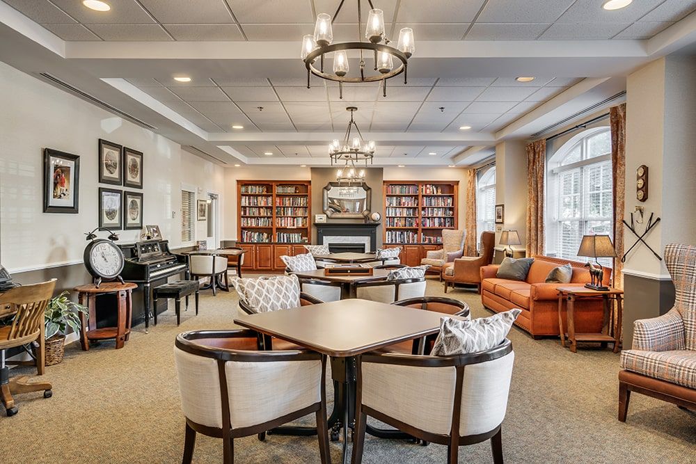 A cozy library reading room with comfortable seating, surrounded by bookshelves, featuring elegant chandeliers and a fireplace.