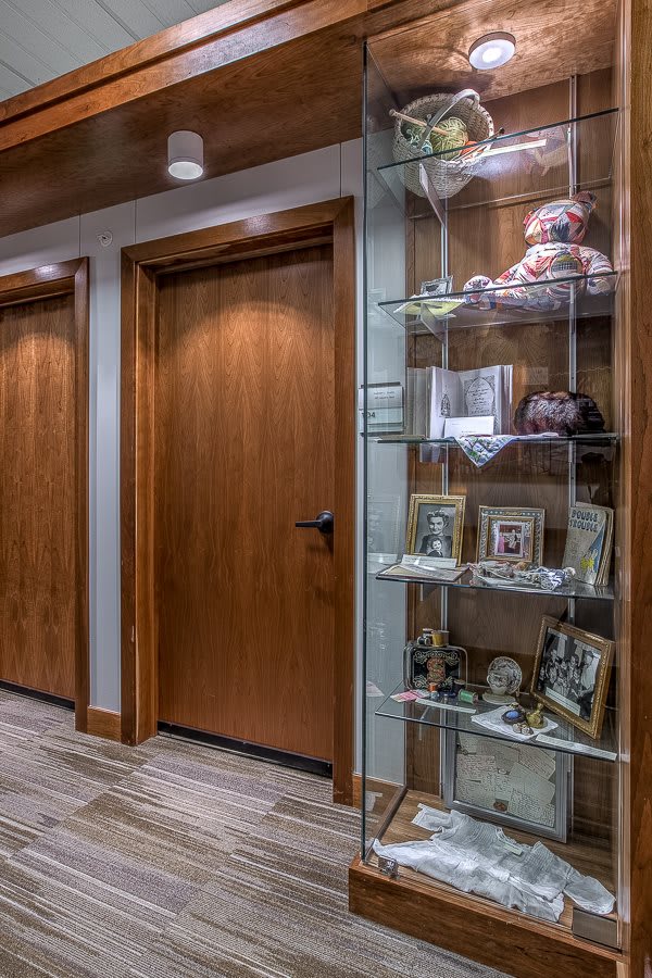 A hallway with wooden doors and a glass display cabinet showcasing framed photos and decorative items.