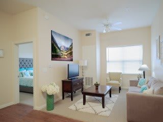 A bright and well-decorated living room with a view into a bedroom, featuring modern furniture and decor.