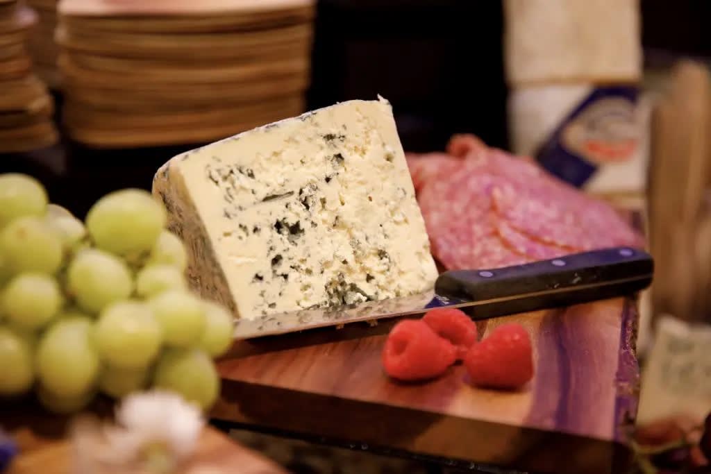 A charcuterie board featuring blue cheese, grapes, raspberries, and salami.
