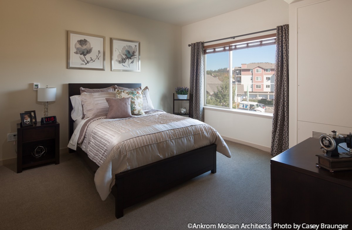 A cozy bedroom with a neatly made bed, large window, and decorative artwork on the wall.