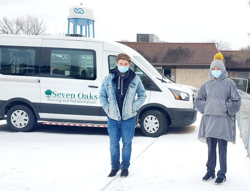 Two individuals standing in the snow beside a transportation van from Seven Oaks.