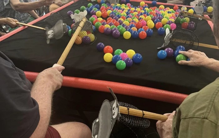 People playing an indoor table game using sticks to hit colorful balls.