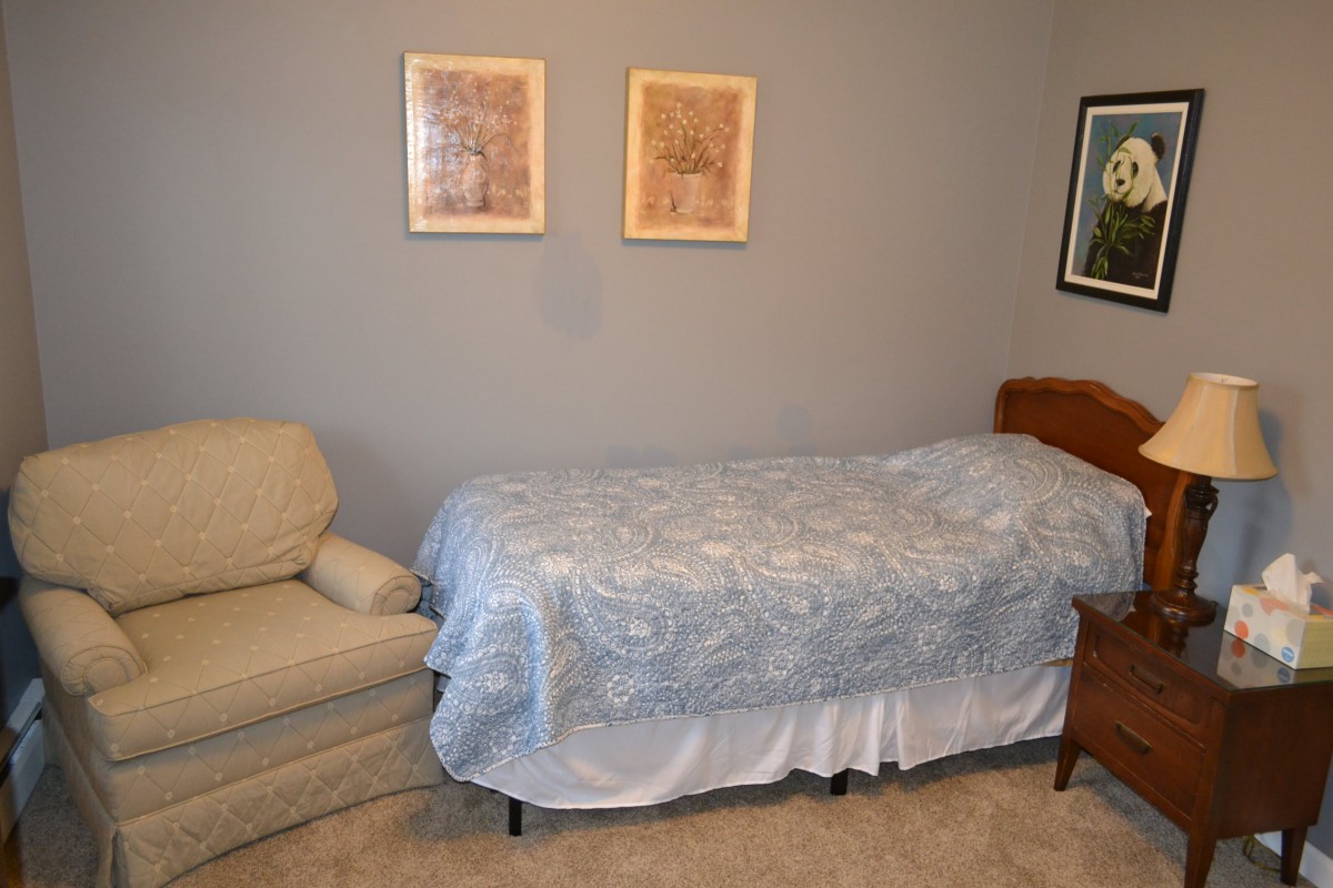 A simple bedroom with a bed, chair, and wall art.