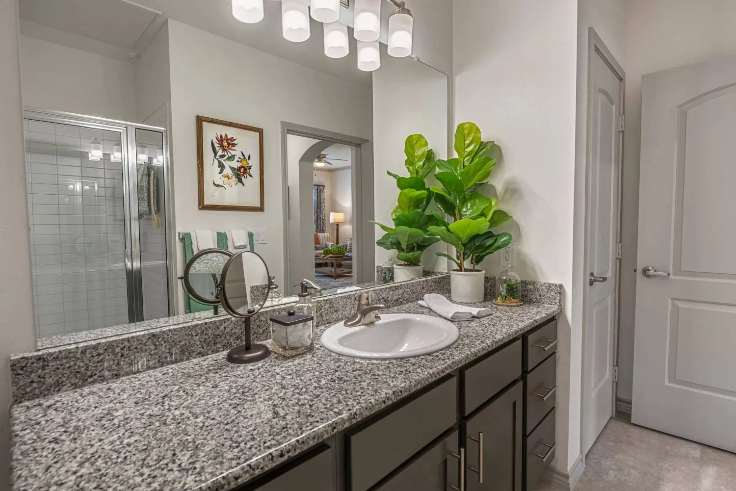 A modern bathroom with a granite countertop, decorative plants, and stylish lighting.