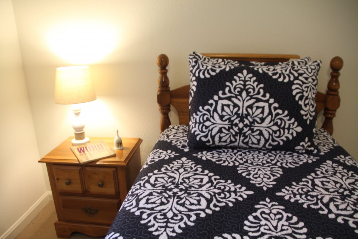 A cozy bedroom scene featuring a wooden bed with patterned bedding and a bedside lamp illuminating the nightstand.