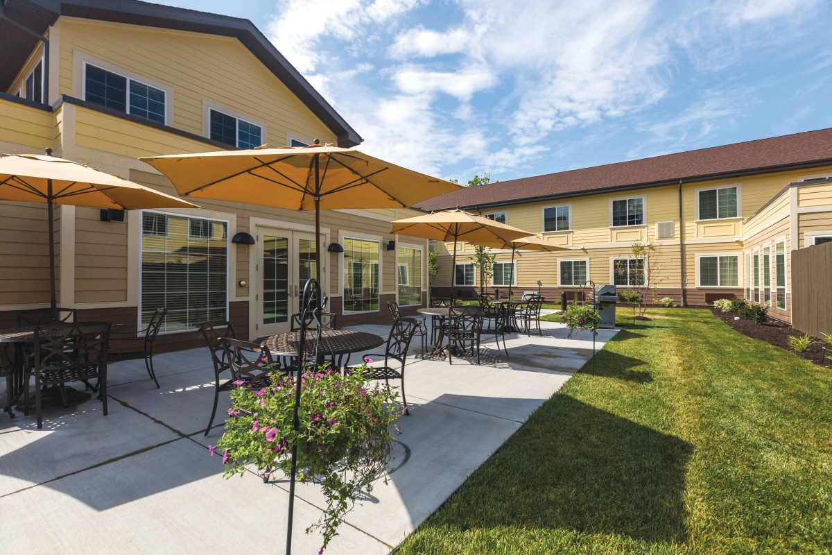 A sunny patio with tables, chairs, and umbrellas outside a beige building.