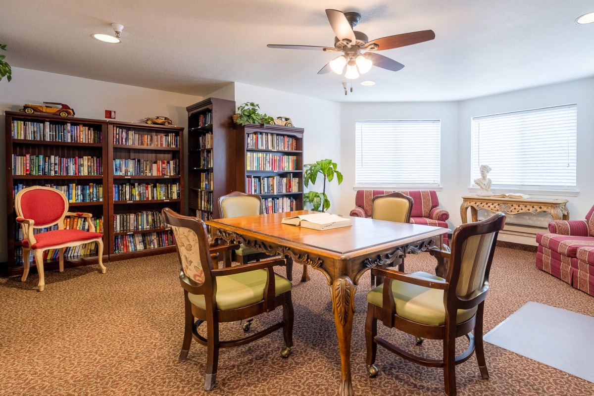 A cozy reading room with bookshelves, a wooden table, and chairs.