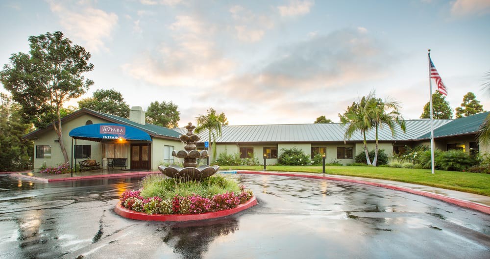 The exterior view of a hotel features a landscaped entrance with a central fountain.