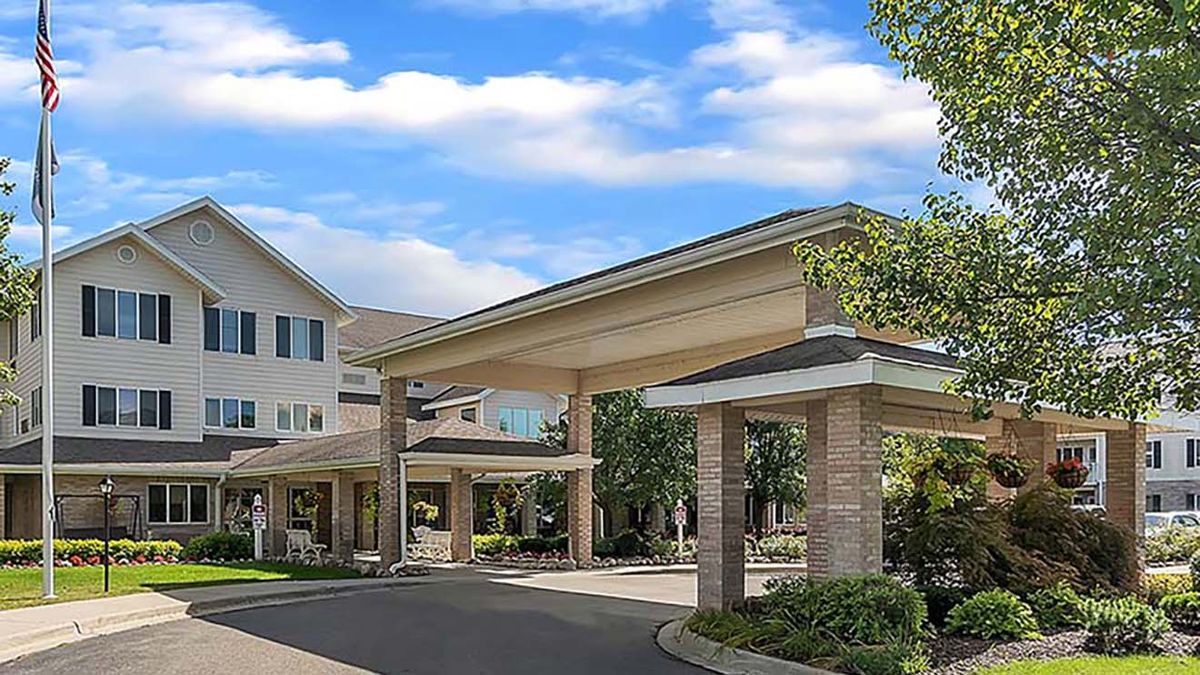 A building entrance with a canopy and surrounding trees under a partly cloudy sky.