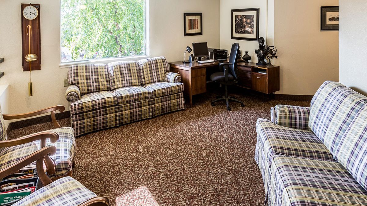 A cozy living room office space with plaid sofas, a desk, and a window.