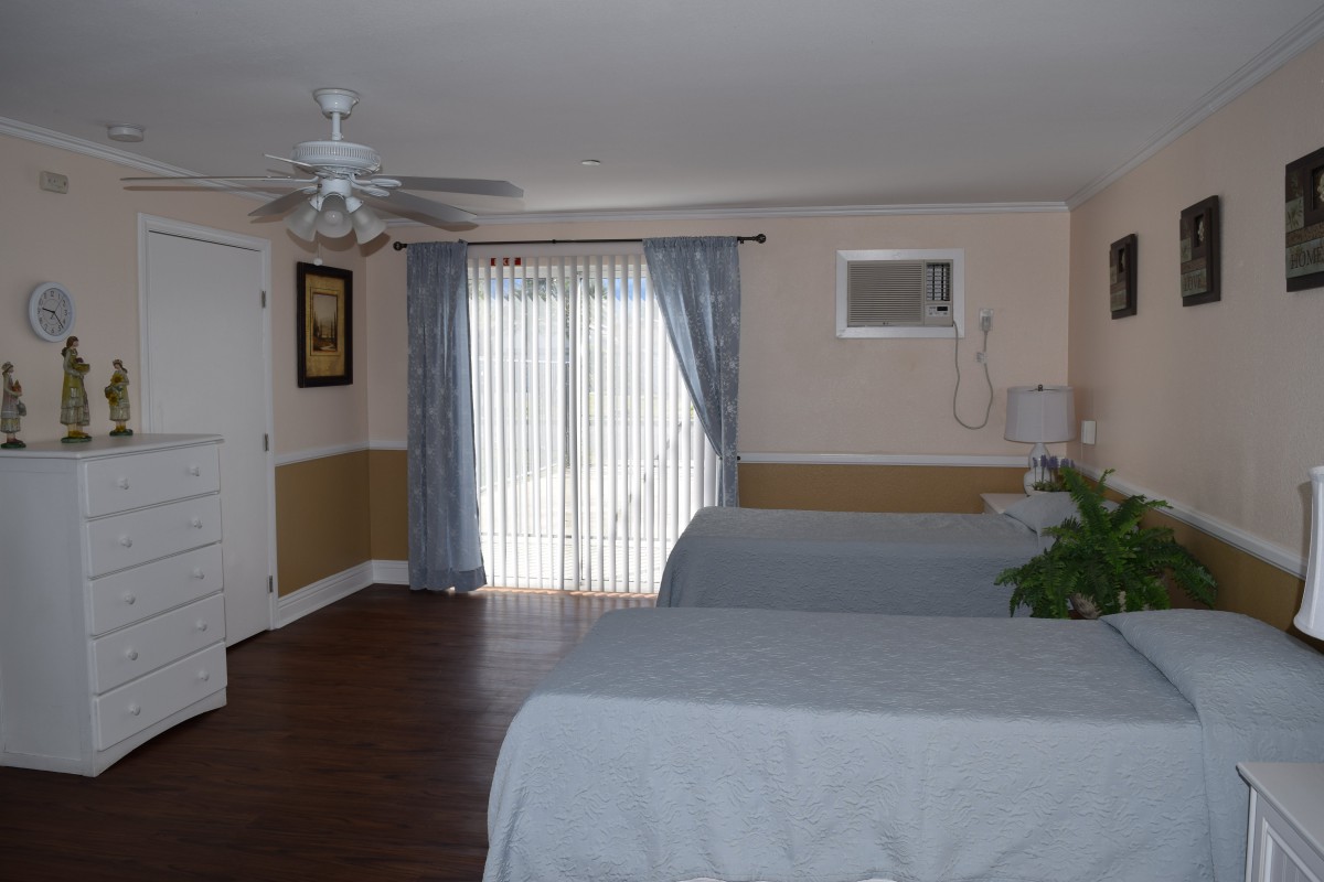 A spacious bedroom with two beds, ceiling fan, and large sliding glass doors with curtains.