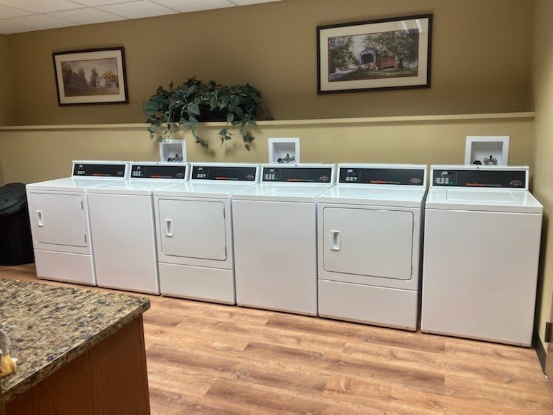 A clean and organized laundry room with several washing machines and dryers lined up against the wall.