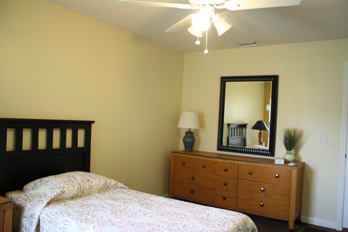 A simple bedroom with a bed, dresser, mirror, and lamp.