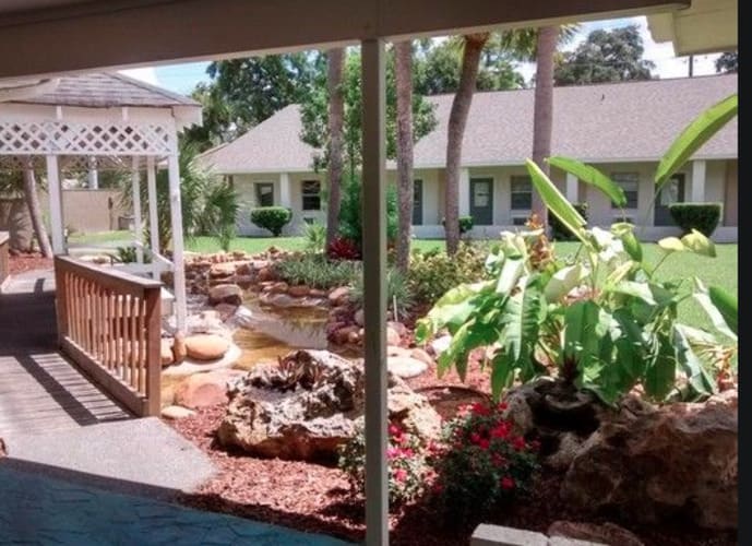 A serene garden view with a gazebo, pond, and tropical plants.