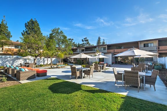 A sunny outdoor patio area with chairs, tables, and surrounding garden greenery.