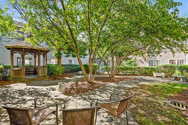 A peaceful garden setting with a gazebo and chairs under the shade of trees.