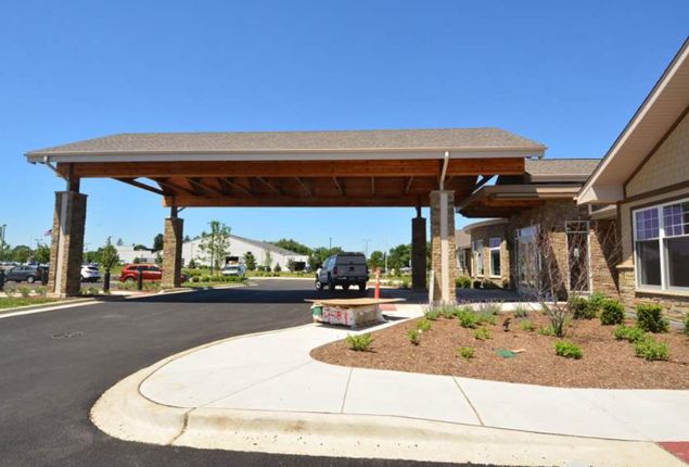 A modern building entrance with a wide carport and landscaped driveway.
