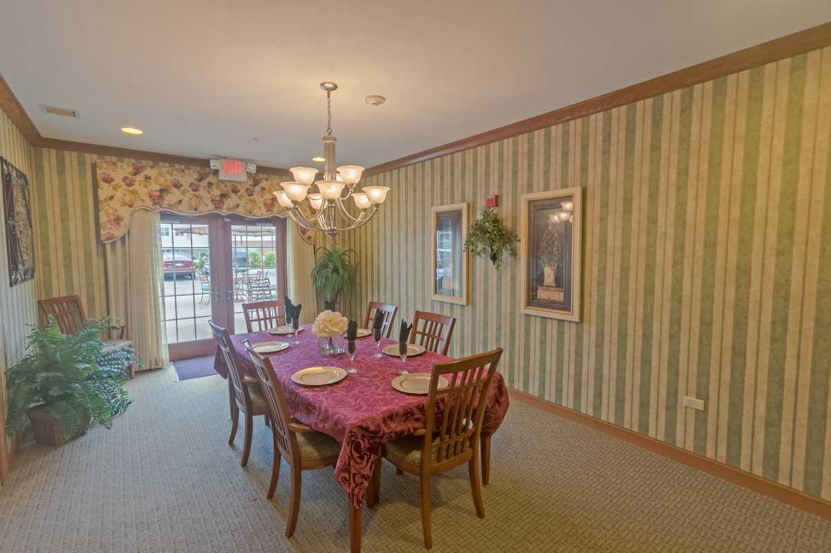 A cozy dining room with a table set for a meal, featuring elegant wallpaper and a chandelier.