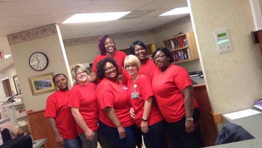 A cheerful group of women wearing red shirts, posing together indoors.