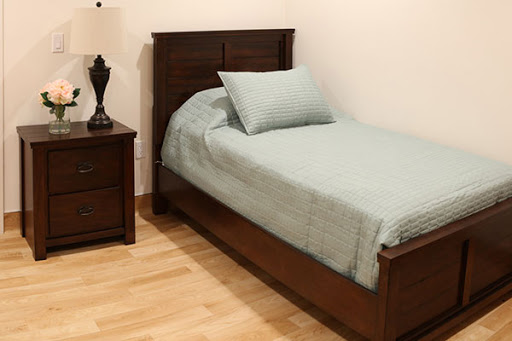 A cozy bedroom setup featuring a single bed with teal bedding and a matching nightstand with a lamp.