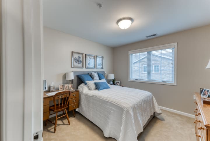 A cozy bedroom with a neatly made bed, a wooden desk, and framed artwork on the walls.