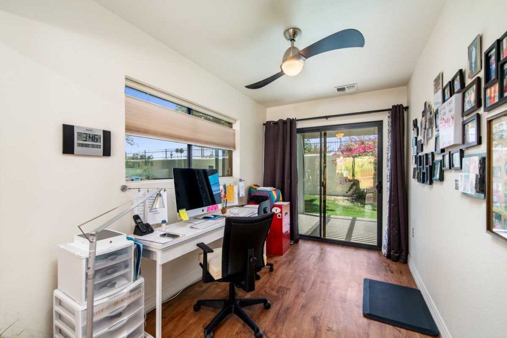A modern home office with a desk and computer, featuring large windows and a sliding door leading to a garden.