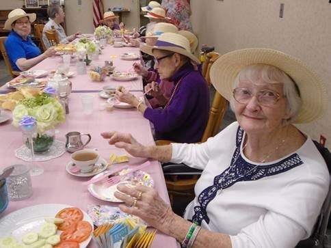 A group of elderly individuals enjoying a tea party, wearing hats and seated at a decorated table.
