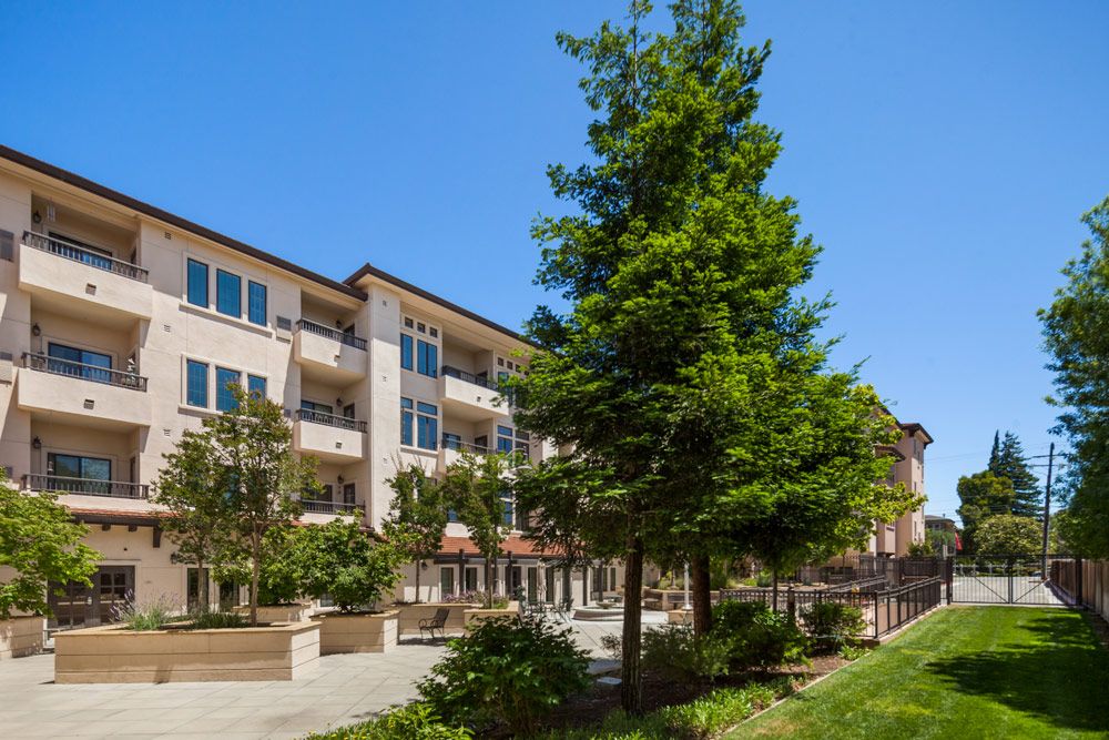 A residential apartment building with surrounding greenery under a clear blue sky.