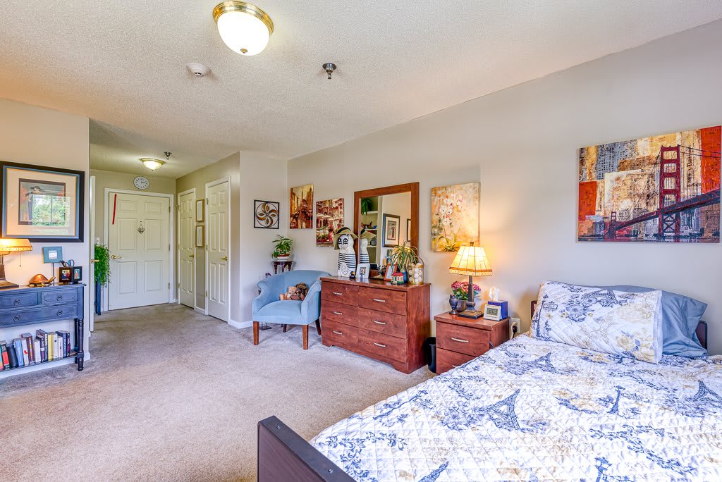 A cozy bedroom with a neatly arranged bed, dresser, and various artworks on the walls.