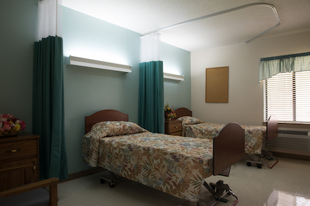 A hospital room featuring two beds with patterned bedding and privacy curtains.