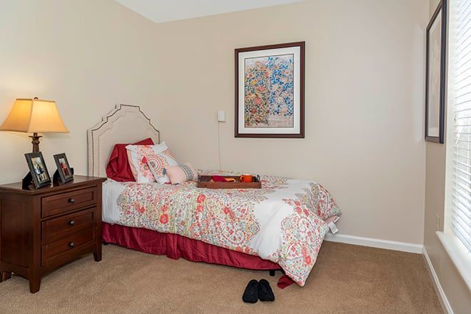 A cozy bedroom with a single bed adorned with a colorful bedspread, next to a wooden nightstand and framed artwork on the wall.