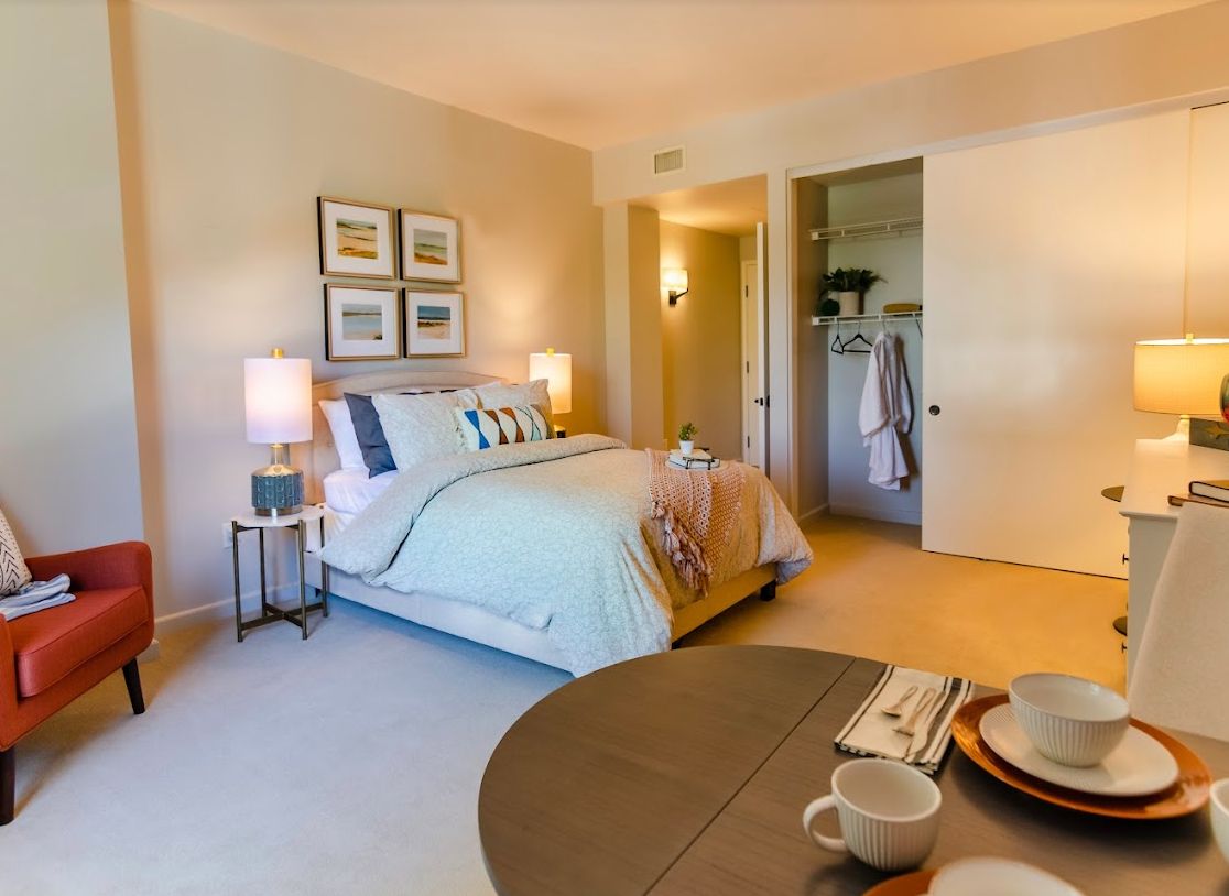 A cozy bedroom interior with a neatly made bed, soft lighting from bedside lamps, and an open closet.