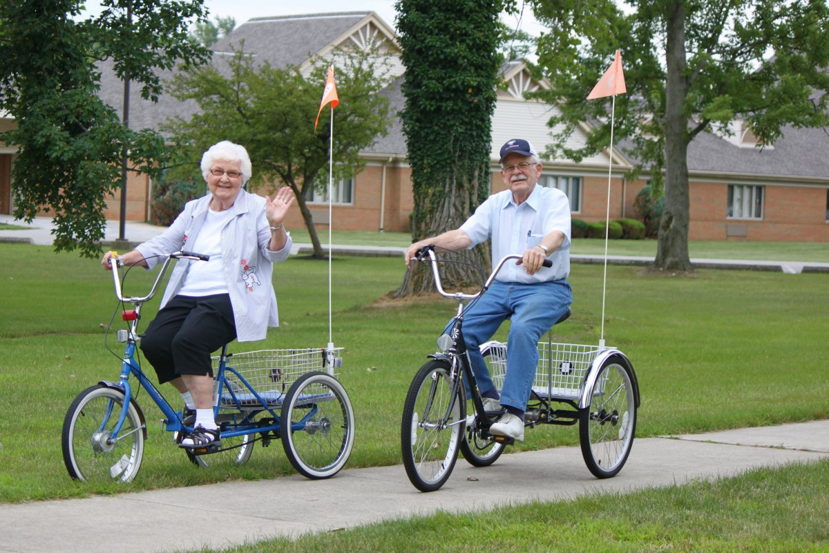 An elderly couple enjoying a leisurely ride on tricycles in a park.
