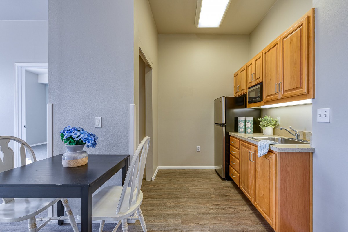 A modern kitchen with wooden cabinets, a refrigerator, and a small dining area with a table and chairs.