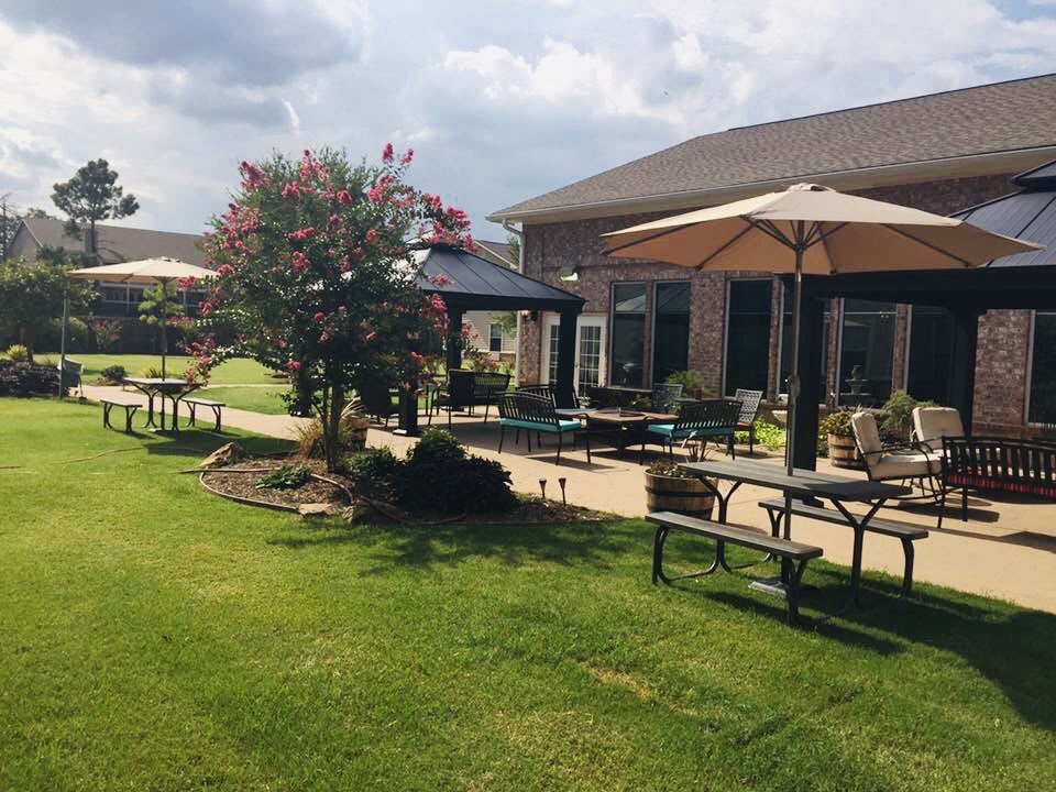 A peaceful garden patio with tables, chairs, and umbrellas surrounded by well-maintained landscaping.