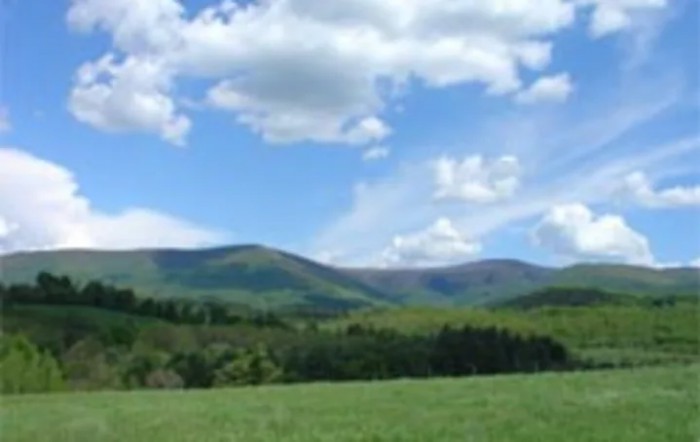 A scenic view of lush green hills and mountains under a blue sky with fluffy clouds.