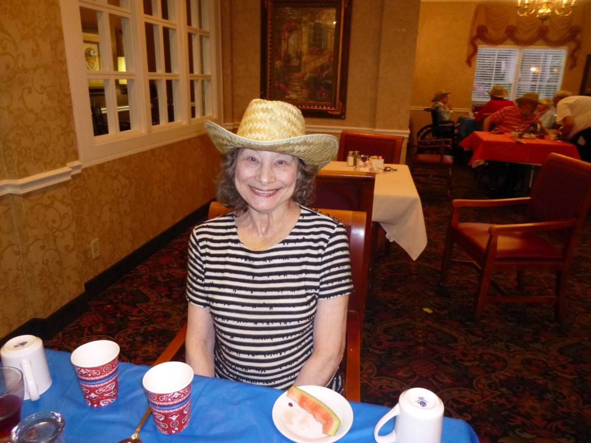 A woman wearing a hat and striped shirt is smiling while seated at a restaurant table.