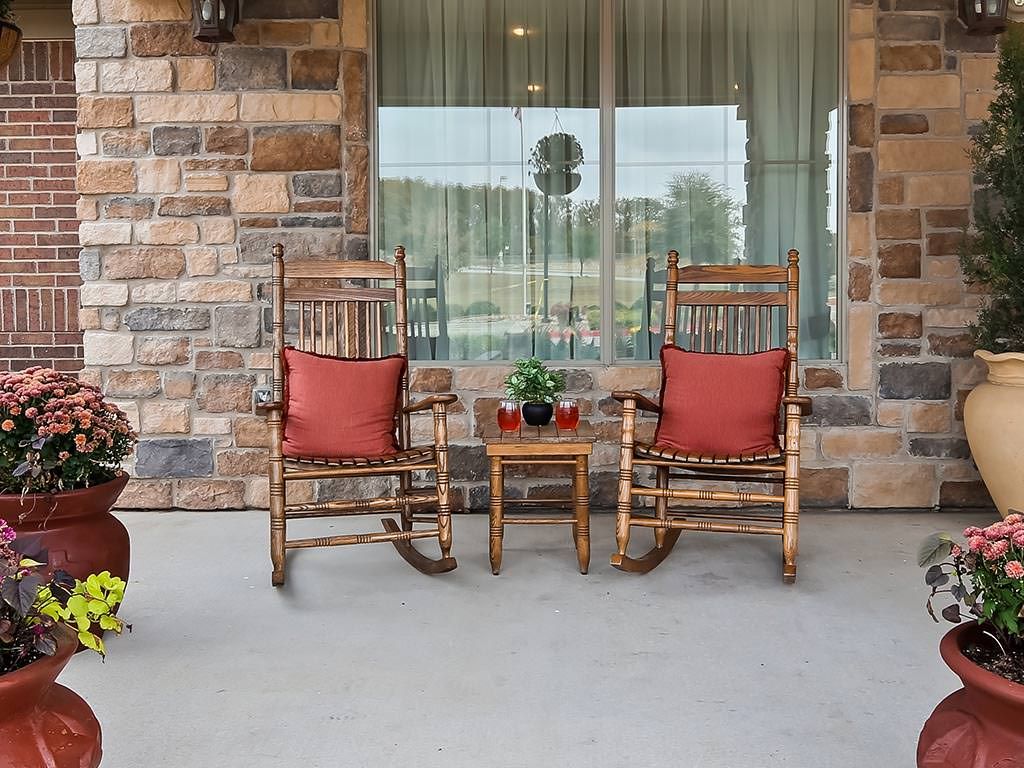Two wooden rocking chairs with red cushions sit on a porch, flanking a small table with a potted plant.